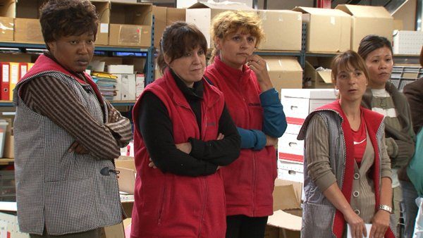 Un groupe d'ouvrière, certaines les bras croisés, dans leur usine.