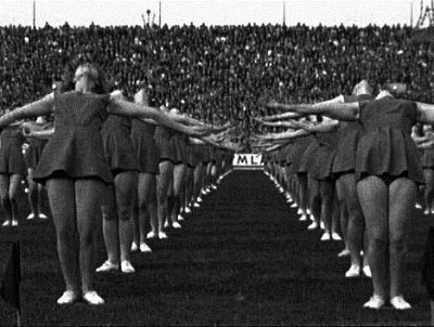 Sur la pelouse d'un stade, sous les regards de milliers de spectateurs, des jeunes filles exécutent une chorégraphie sportive.