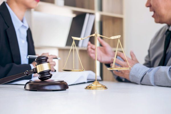 deux personnes en train de discuter autour d'une table avec une balance et un marteau (symbole de la justice)