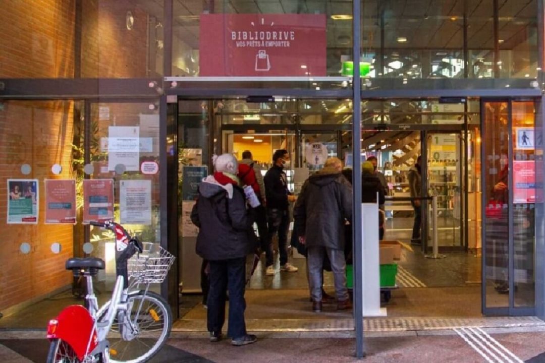 Photo de l'entrée d'une bibliothèque avec des usagers entrant et sortant.